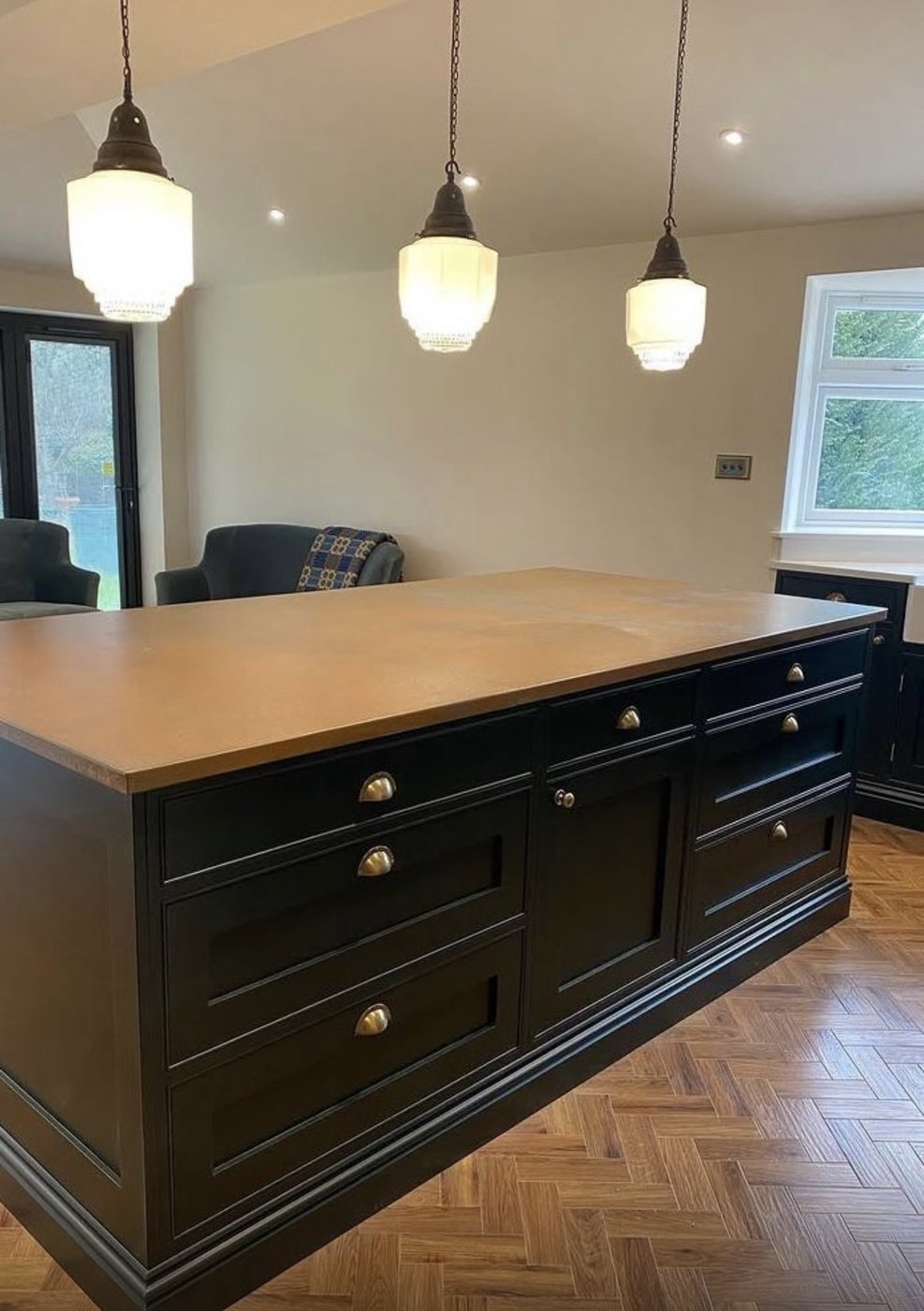 Black painted kitchen island with art deco glass pendants over herringbone parquet