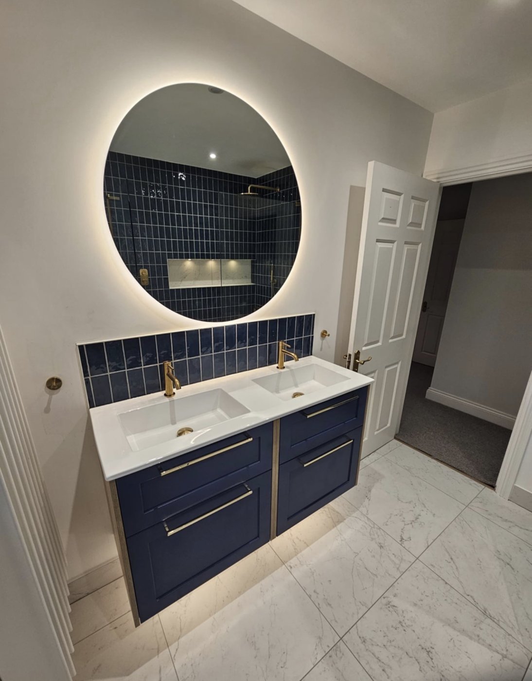 Navy-tiled bathroom with halo backlit mirror, brass taps and marble flooring